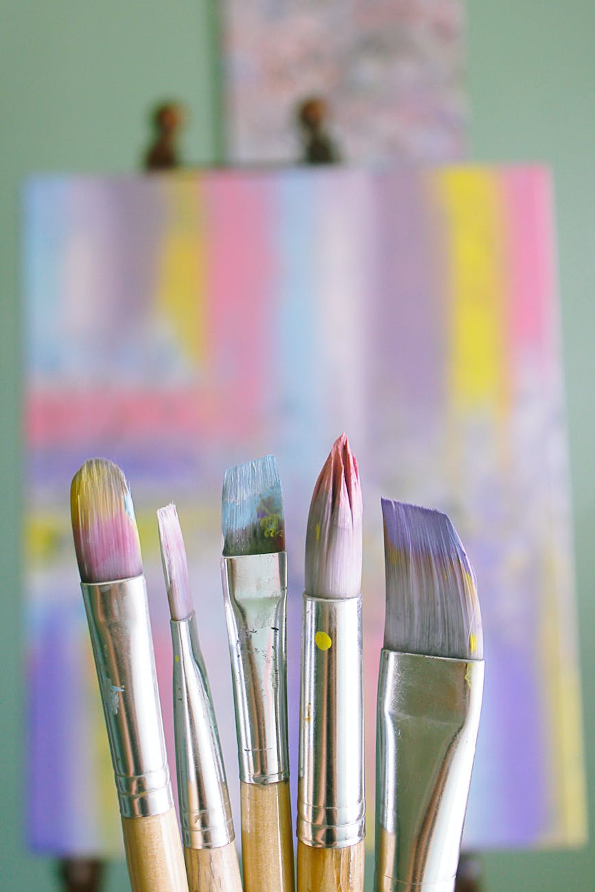 a photo of some used paintbrushes in front of an out of focus painted canvas